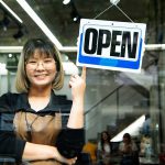 Happy Asian female happy after a great franchise agreement of her salon shop turning round open sign on a door