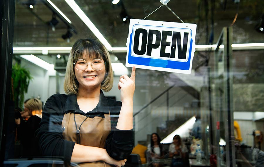 Asian female hairdesser of salon shop turning round open sign on a door