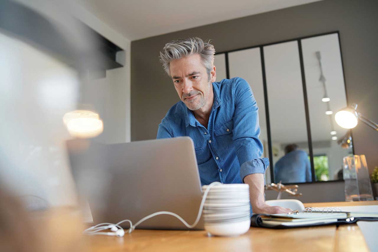 Mature business man working from contemporary home looking on his computer for a work from home policy