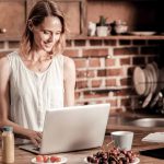 Attractive, cheerful woman looking at the laptop screen from home as she takes advantage of her job's remote work policy.