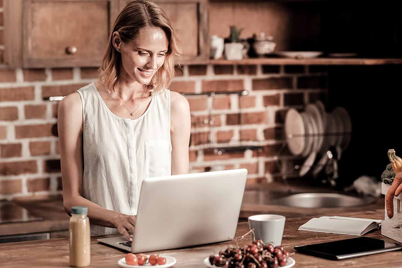 Attractive, cheerful woman looking at the laptop screen from home as she takes advantage of her job's remote work policy.