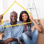 african american couple sitting in what looks like a room of a new house as it is filled with boxes.