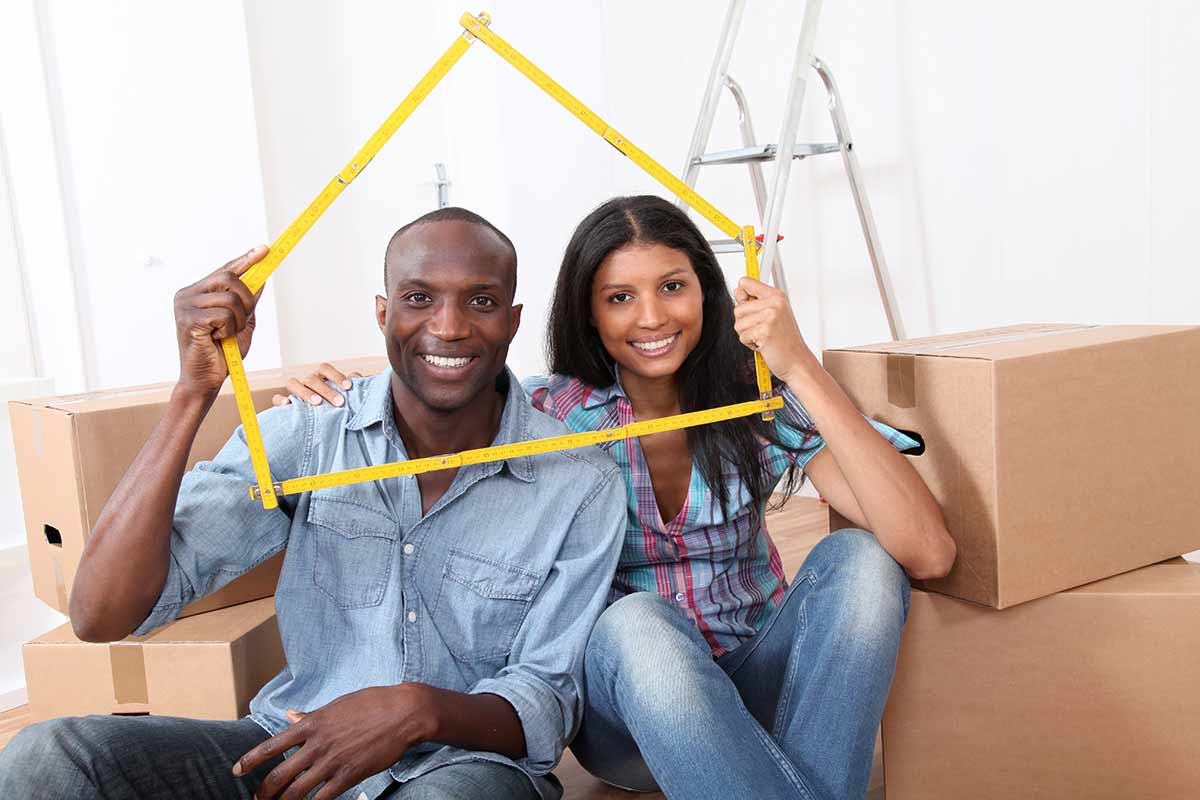 african american couple sitting in what looks like a room of a new house as it is filled with boxes.