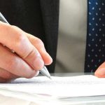 Hands of a man in a suit signing on one of the most important estate planning documents.