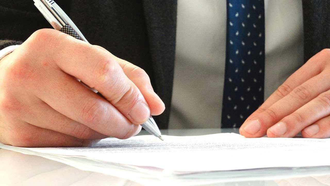 Hands of a man in a suit signing on one of the most important estate planning documents.