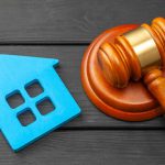 Picture of a gavel sitting on a table next to a tiny model home that suggests you should contact a real estate closing attorney.