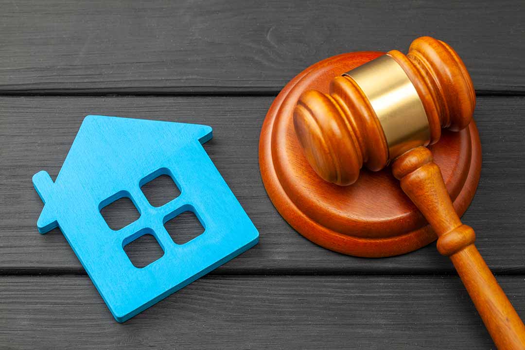 Picture of a gavel sitting on a table next to a tiny model home that suggests you should contact a real estate closing attorney.