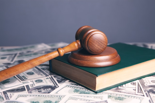 gavel resting on a hardcover book on a bed on 100 dollar bills